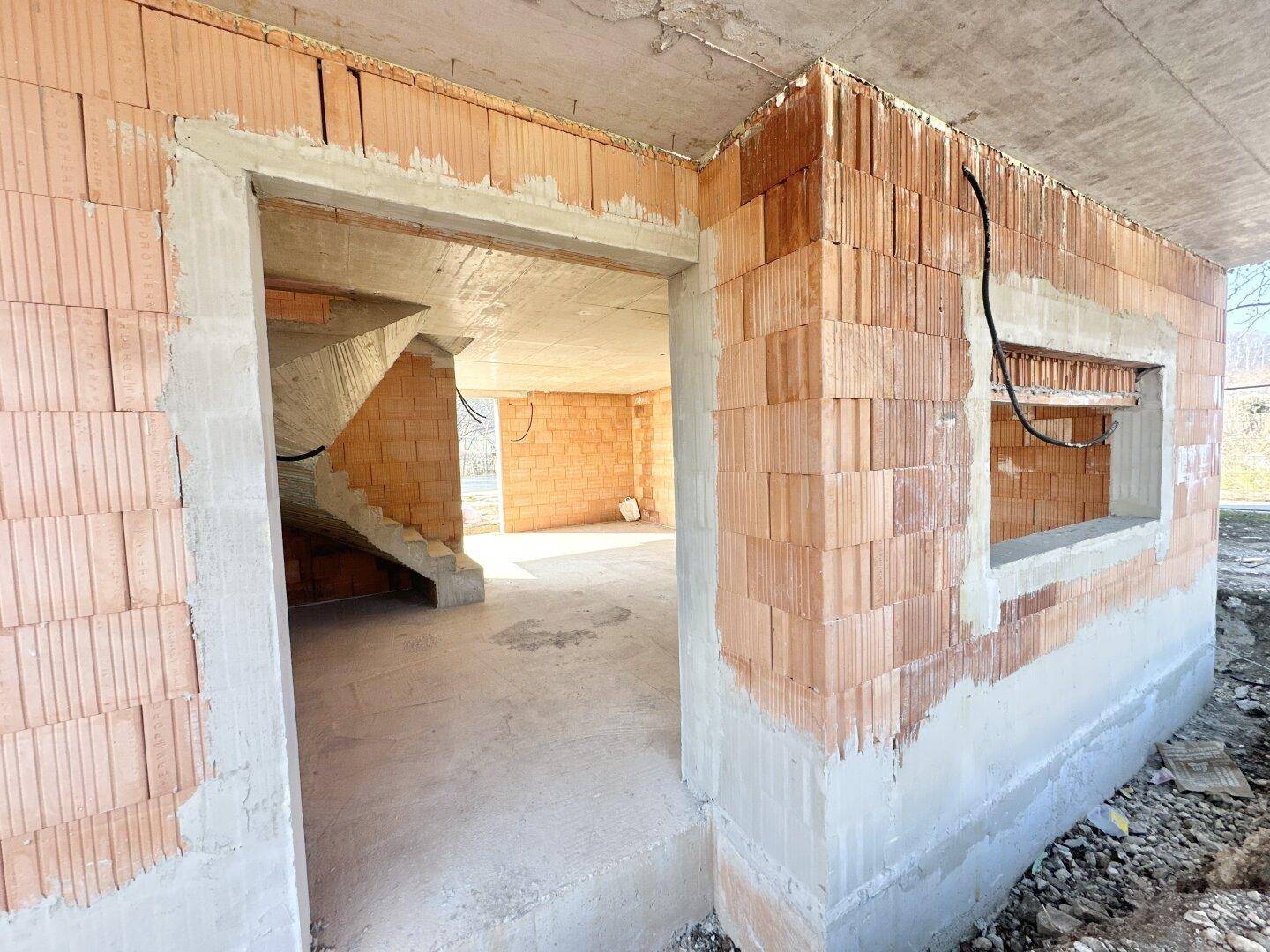 Innenansicht des Rohbaus mit unverputzten Ziegelwänden und Betonboden im Erdgeschoss.