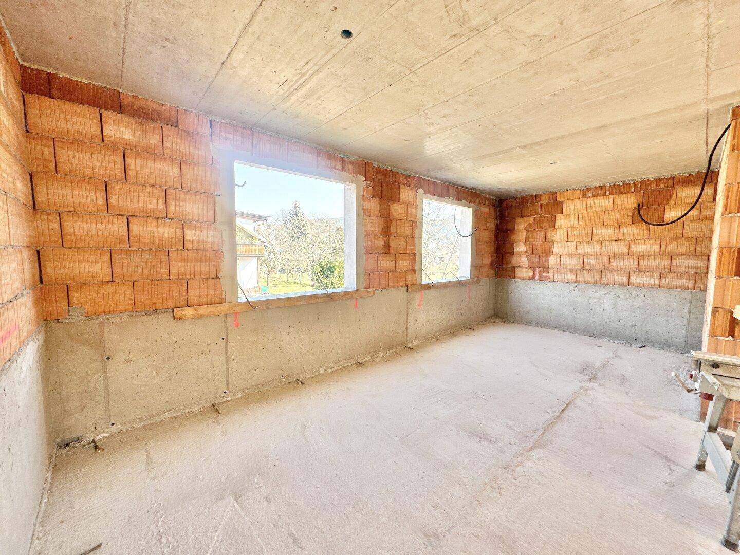 Heller Rohbau-Raum mit zwei großen Fensteröffnungen und Betonboden.