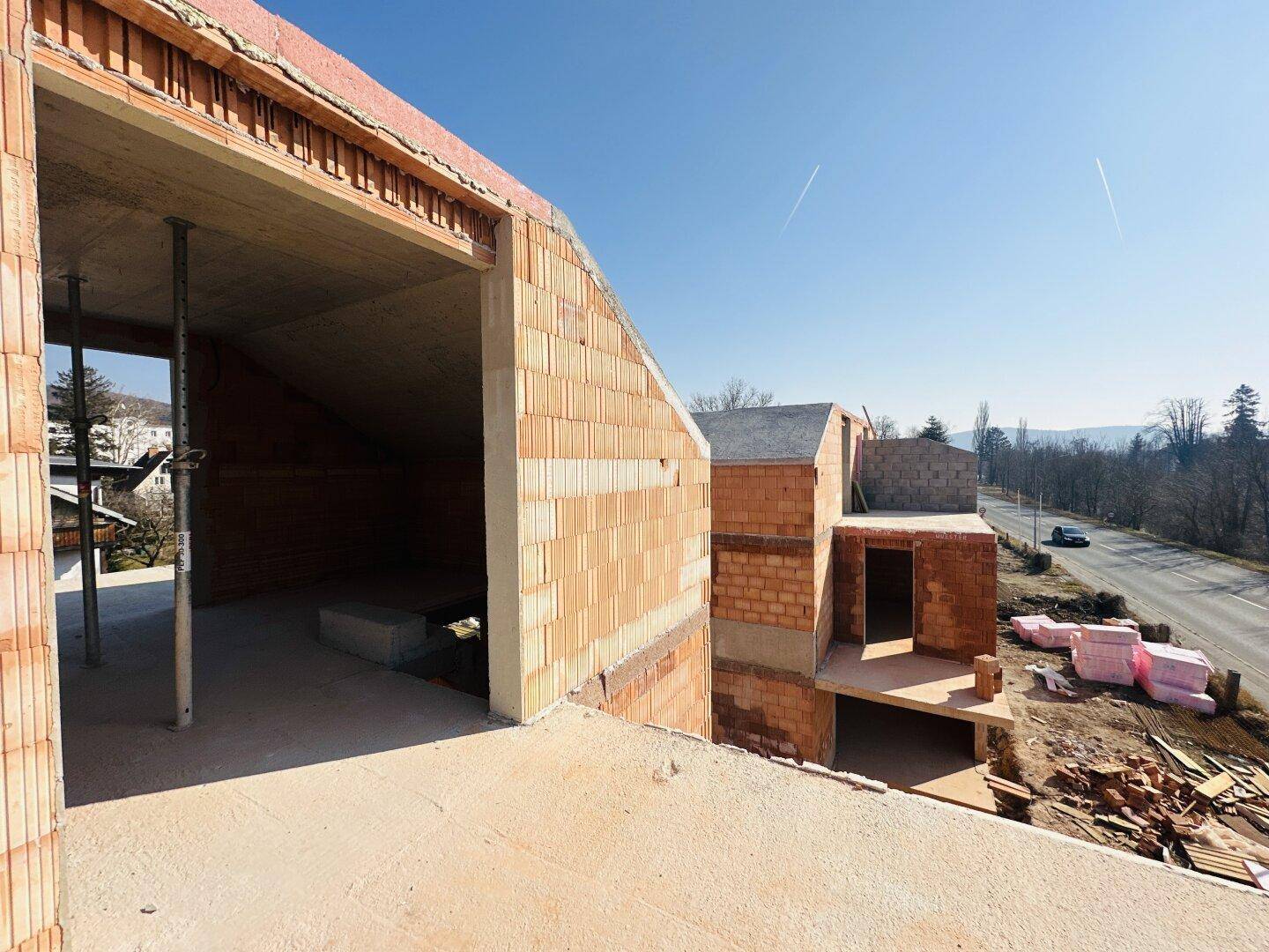 Blick von oben auf die Baustelle und die angrenzende Straße bei strahlendem Wetter.