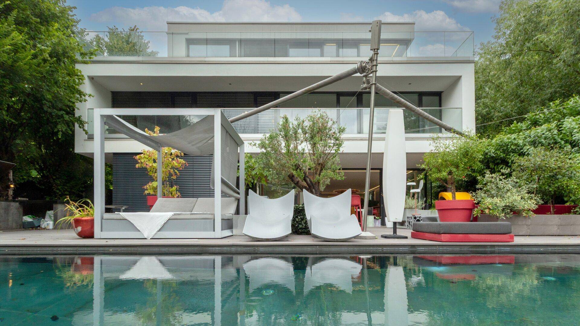 Moderne Villa mit großem Poolbereich, luxuriösen Outdoor-Möbeln und üppiger grüner Umgebung.