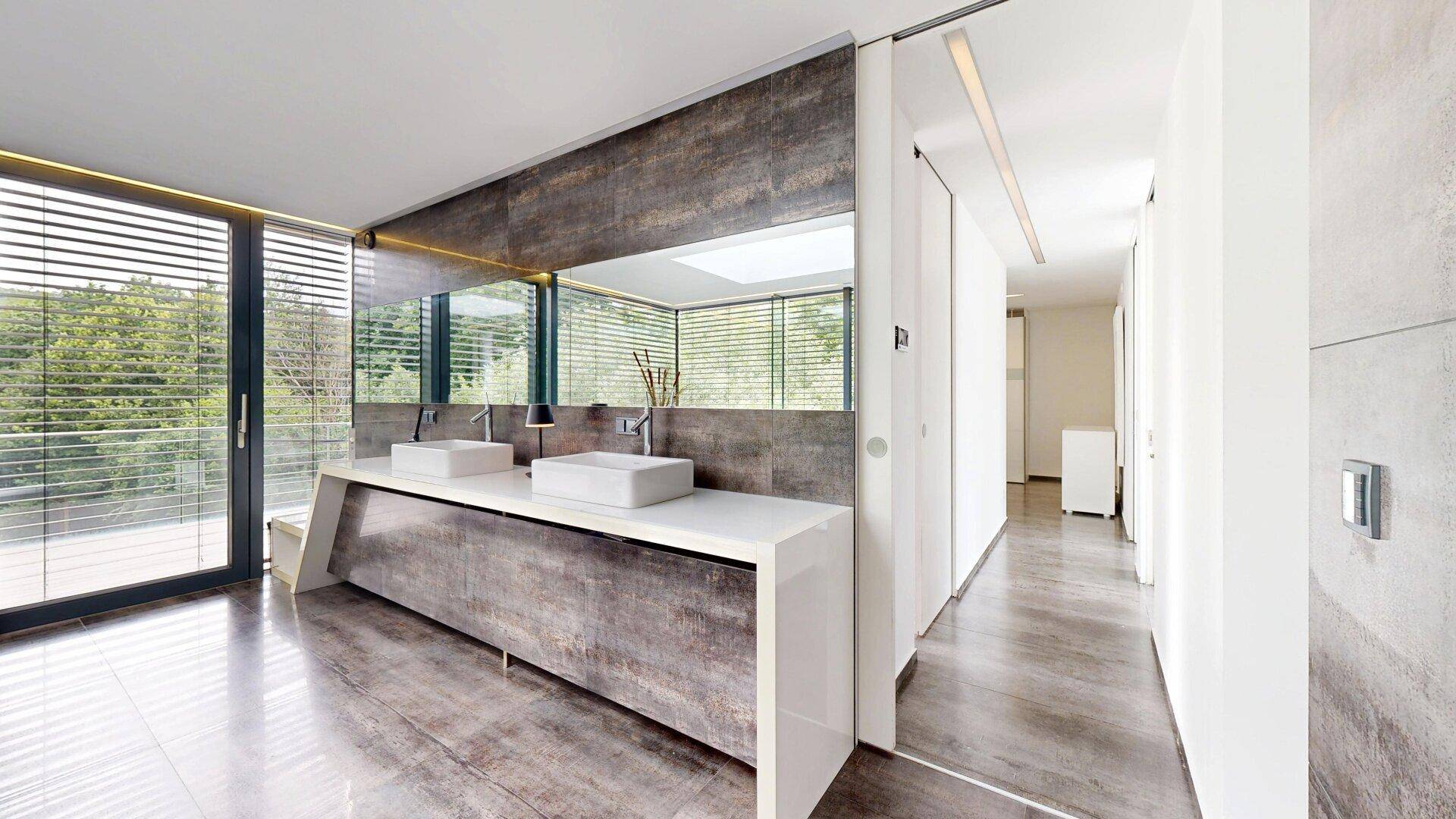 Modernes Badezimmer mit Doppelwaschbecken, großen Fenstern und Blick auf die Natur.