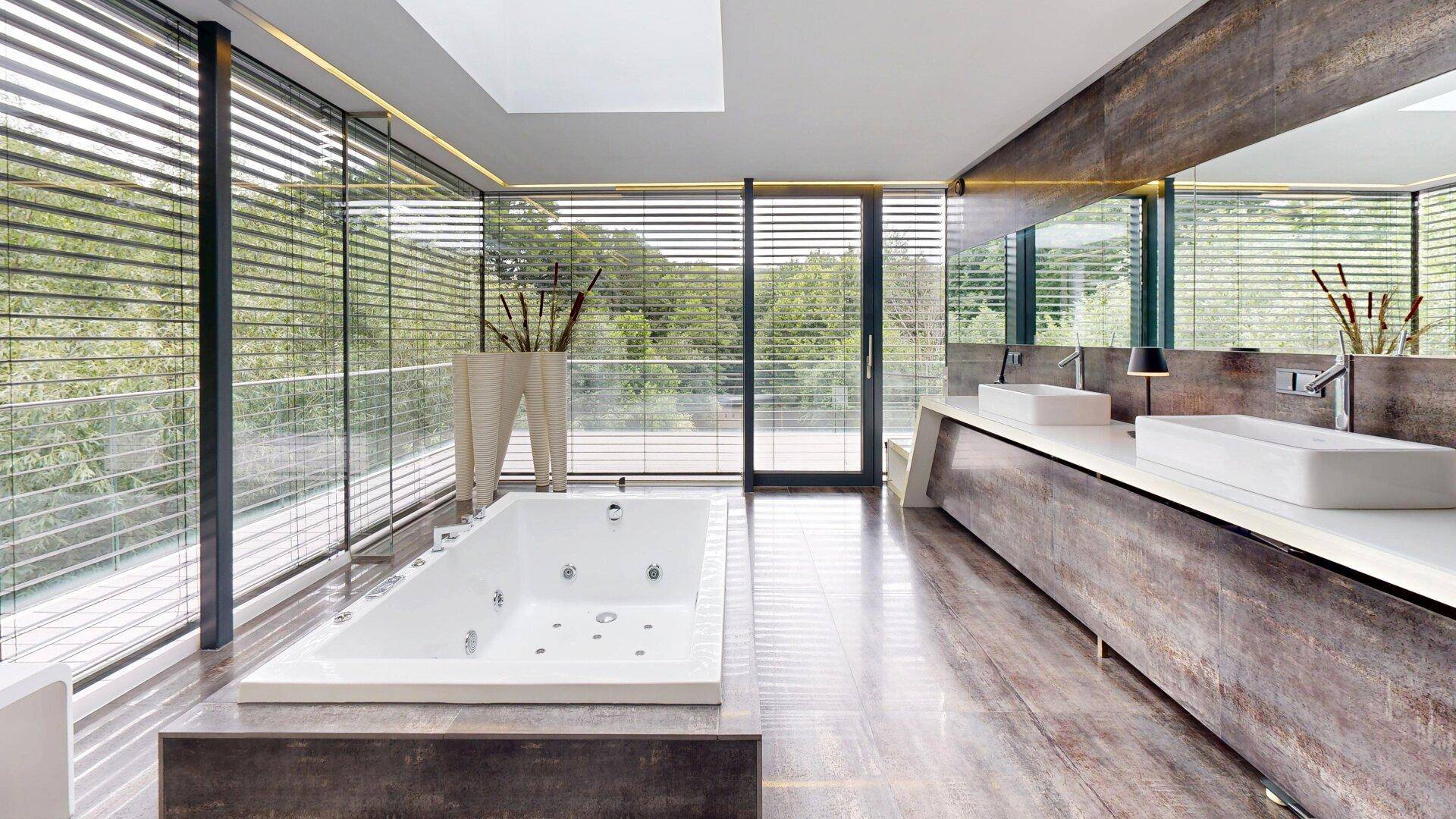 Luxuriöses Badezimmer mit großer Badewanne, Doppelwaschbecken und raumhohen Fenstern mit Jalousien.