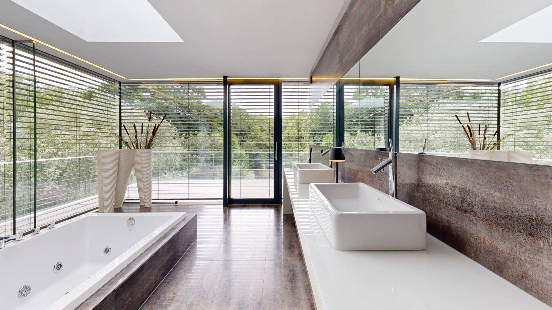 Elegantes Badezimmer mit Whirlpool-Badewanne, zwei Waschbecken und weitem Blick ins Grüne.