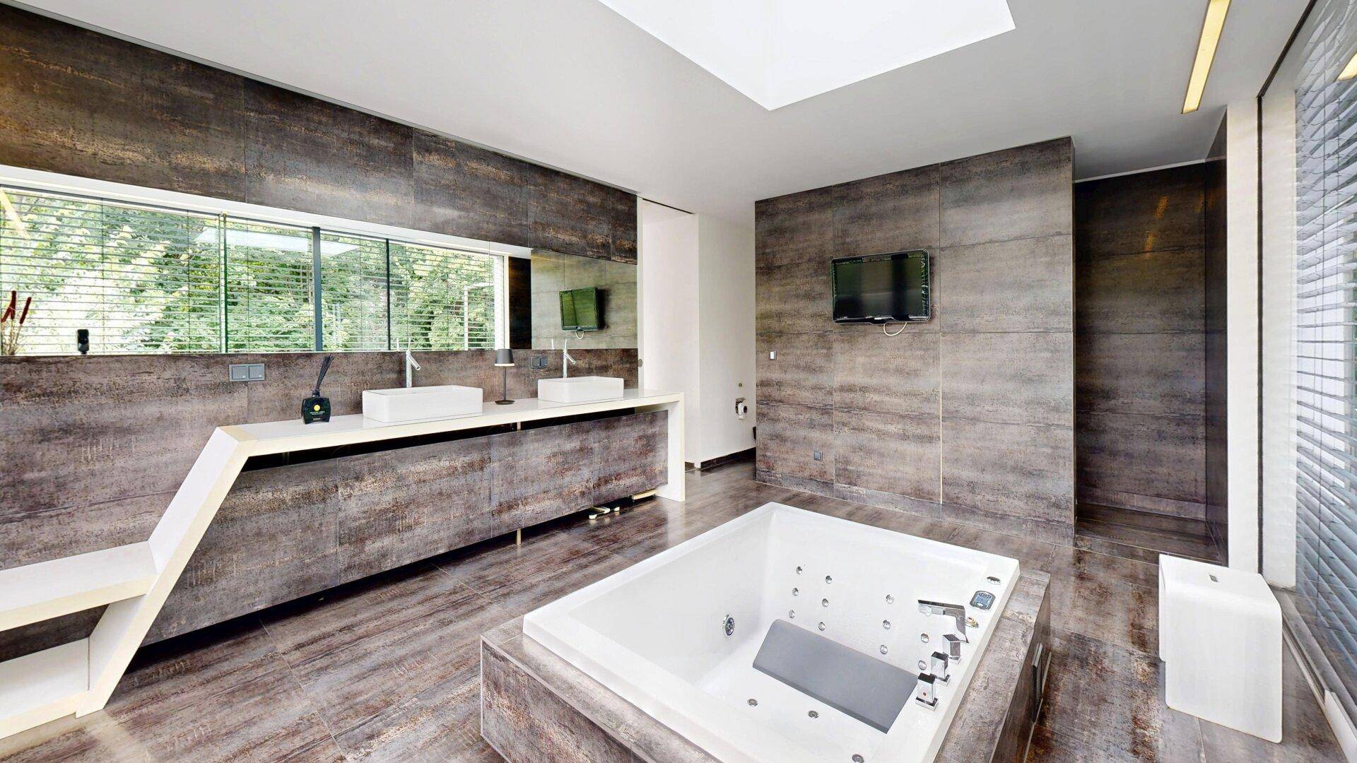Luxuriöses Badezimmer mit eingelassener Badewanne, Doppelwaschbecken und integriertem Fernseher.