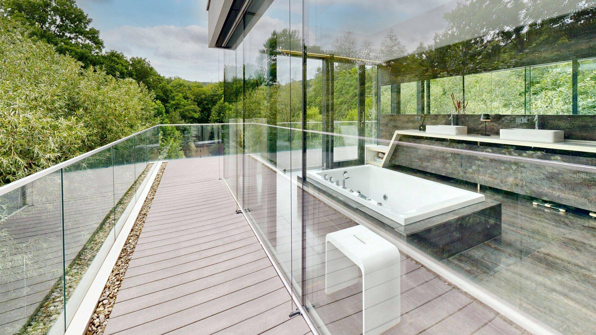 Moderne Terrasse mit Glasgeländer und Einblick in ein luxuriöses Badezimmer mit Badewanne.