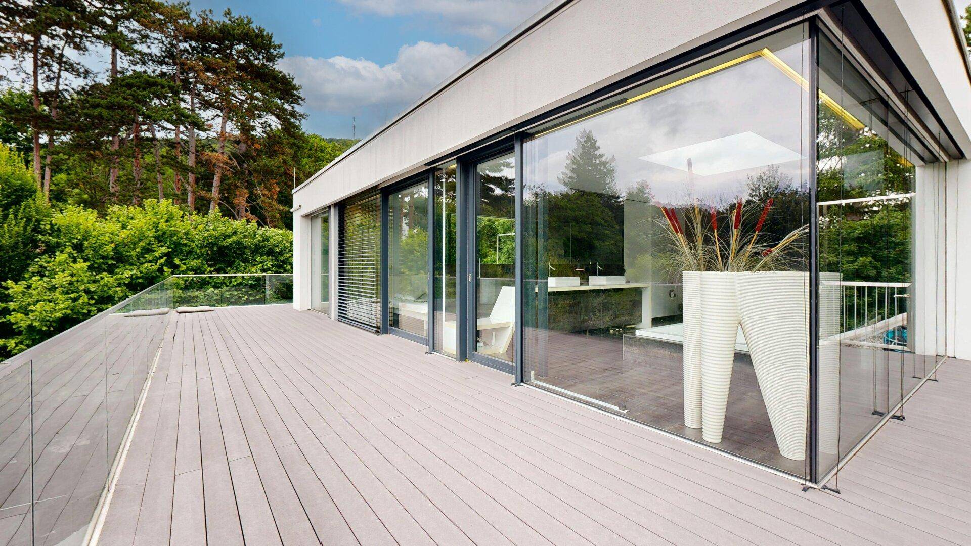 Geräumige Terrasse mit Holzboden und Glasfront, die einen Panoramablick auf die Natur bietet.