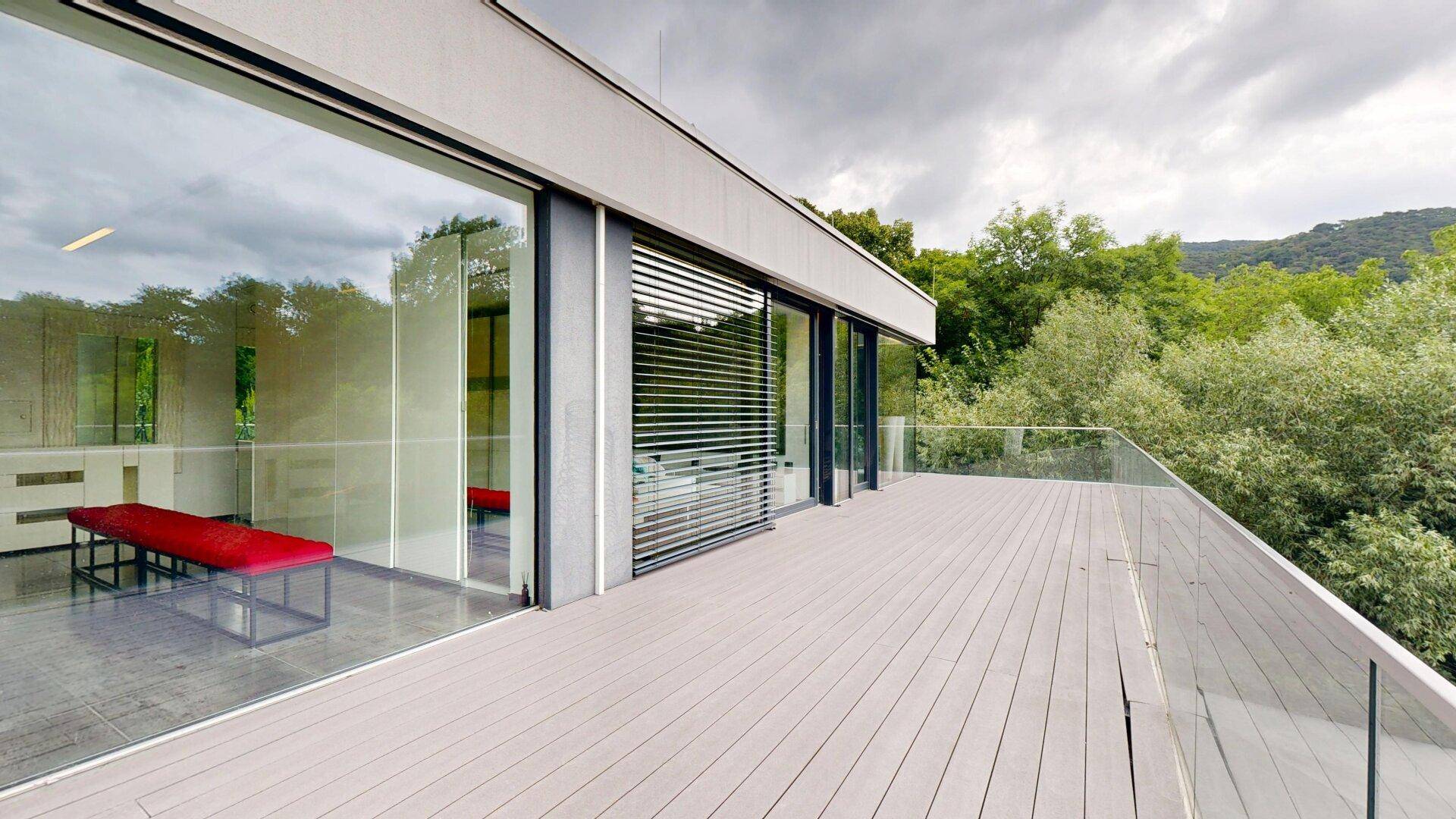 Moderne Terrasse mit Holzboden und Glasgeländer, bietet einen weiten Blick auf die bewaldete Landschaft.