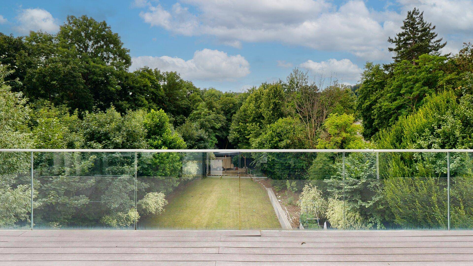 Große Holzterrasse mit Glasgeländer bietet einen weiten Blick ins Grüne und auf den Garten.