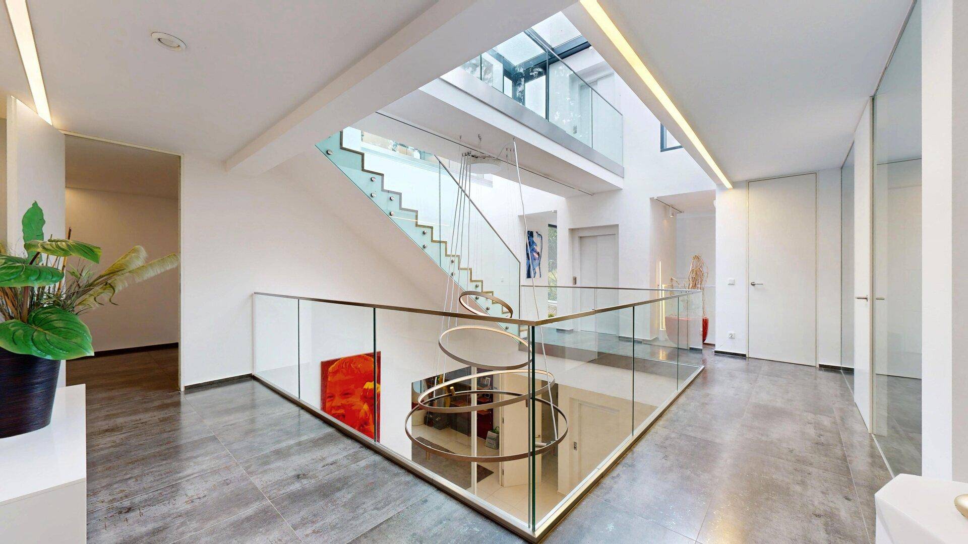 Offener, heller Flur mit moderner Architektur, Glasgeländer und viel Tageslicht.