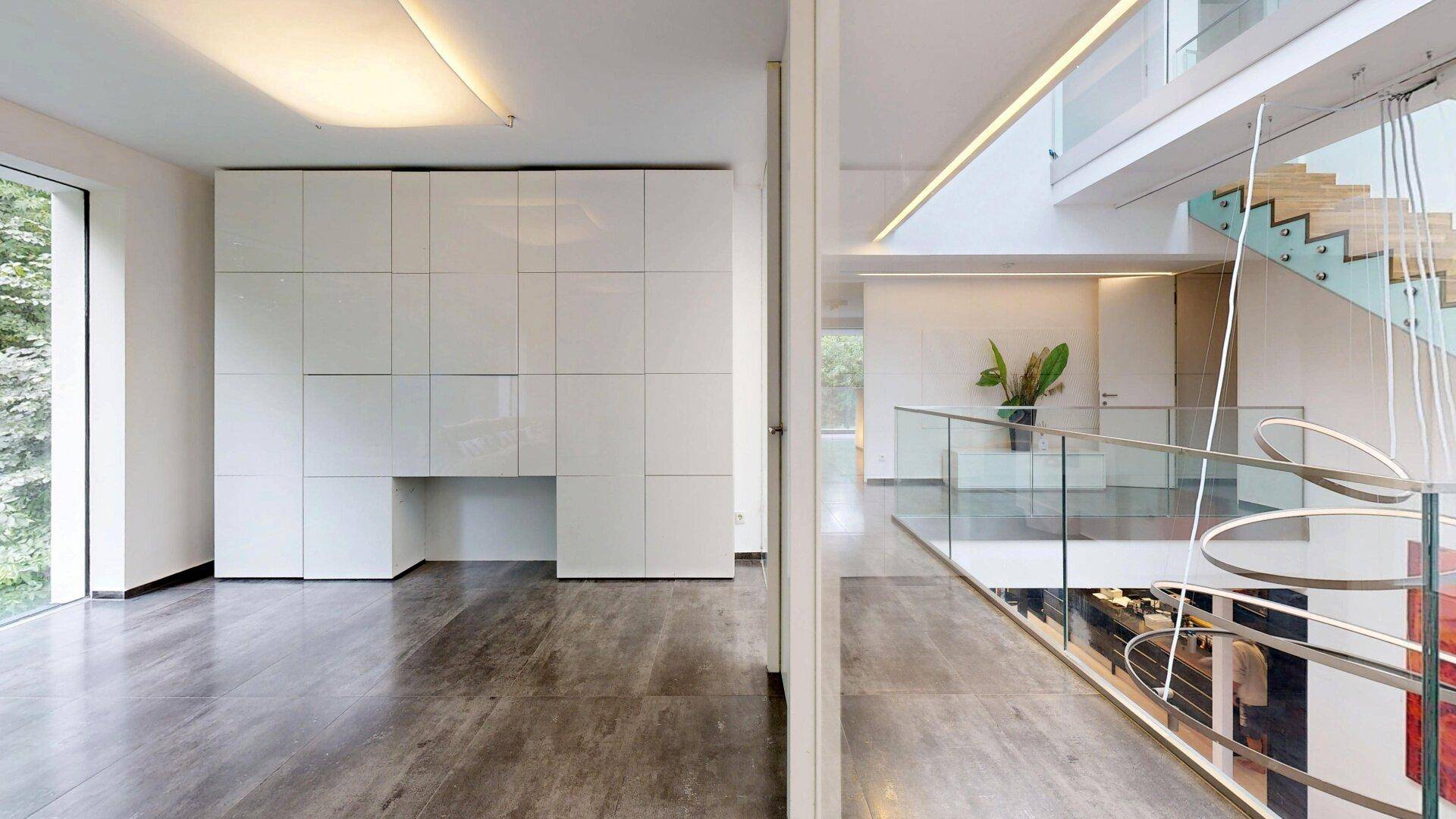 Modernes Wohnzimmer mit großen Fenstern und integrierten Schränken, verbunden mit dem Treppenhaus.
