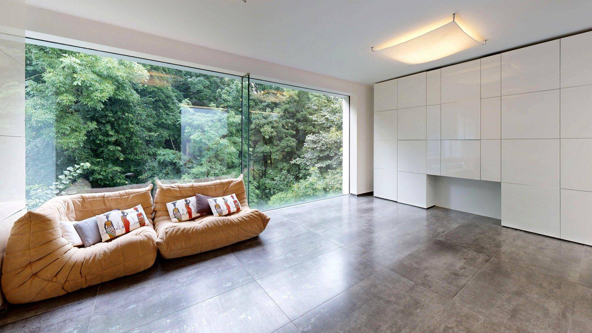 Helles Wohnzimmer mit bodentiefen Fenstern und Blick ins Grüne, ausgestattet mit einem bequemen Sofa.