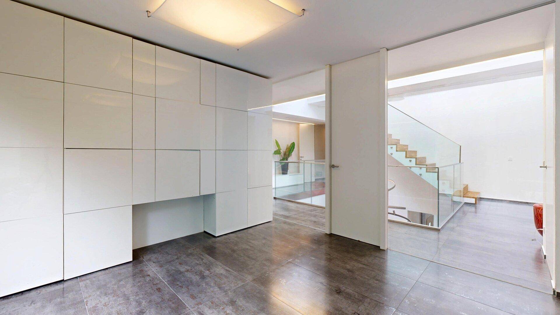 Geräumiges Wohnzimmer mit großen Fenstern und integrierten Schränken, verbunden mit dem Treppenhaus.