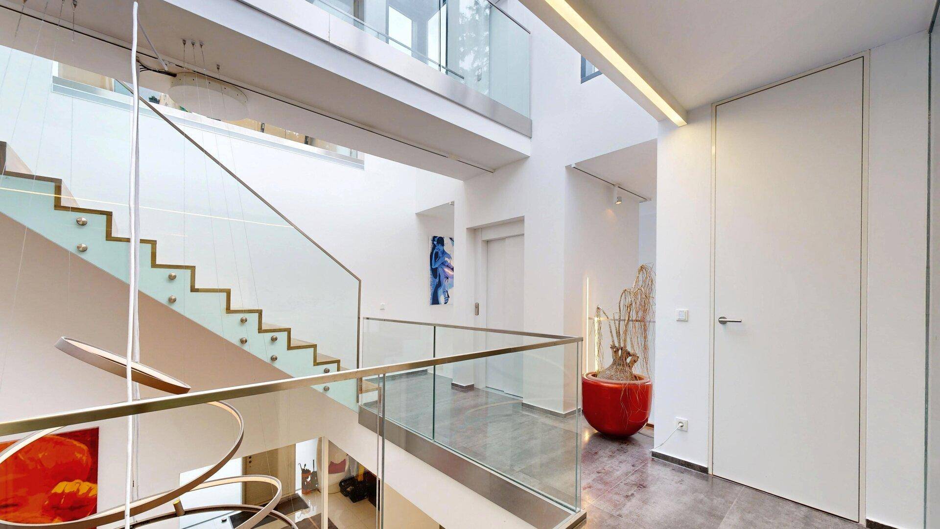 Moderner Flur mit Aufzug, eleganter Holztreppe und Glasgeländer, hell und offen gestaltet.