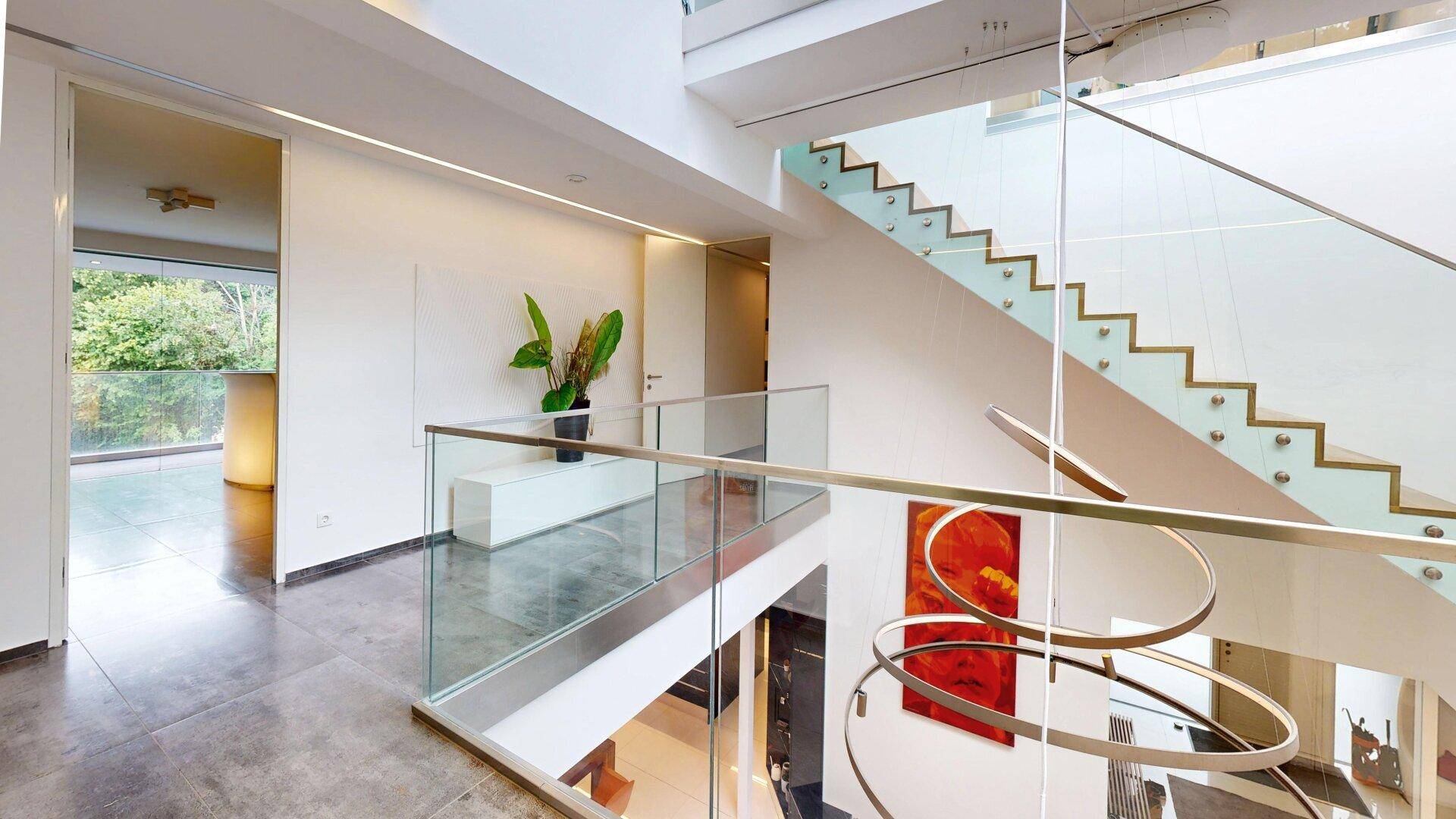 Heller Flur mit moderner Treppe, Glasgeländer und Blick auf den angrenzenden Wohnbereich.