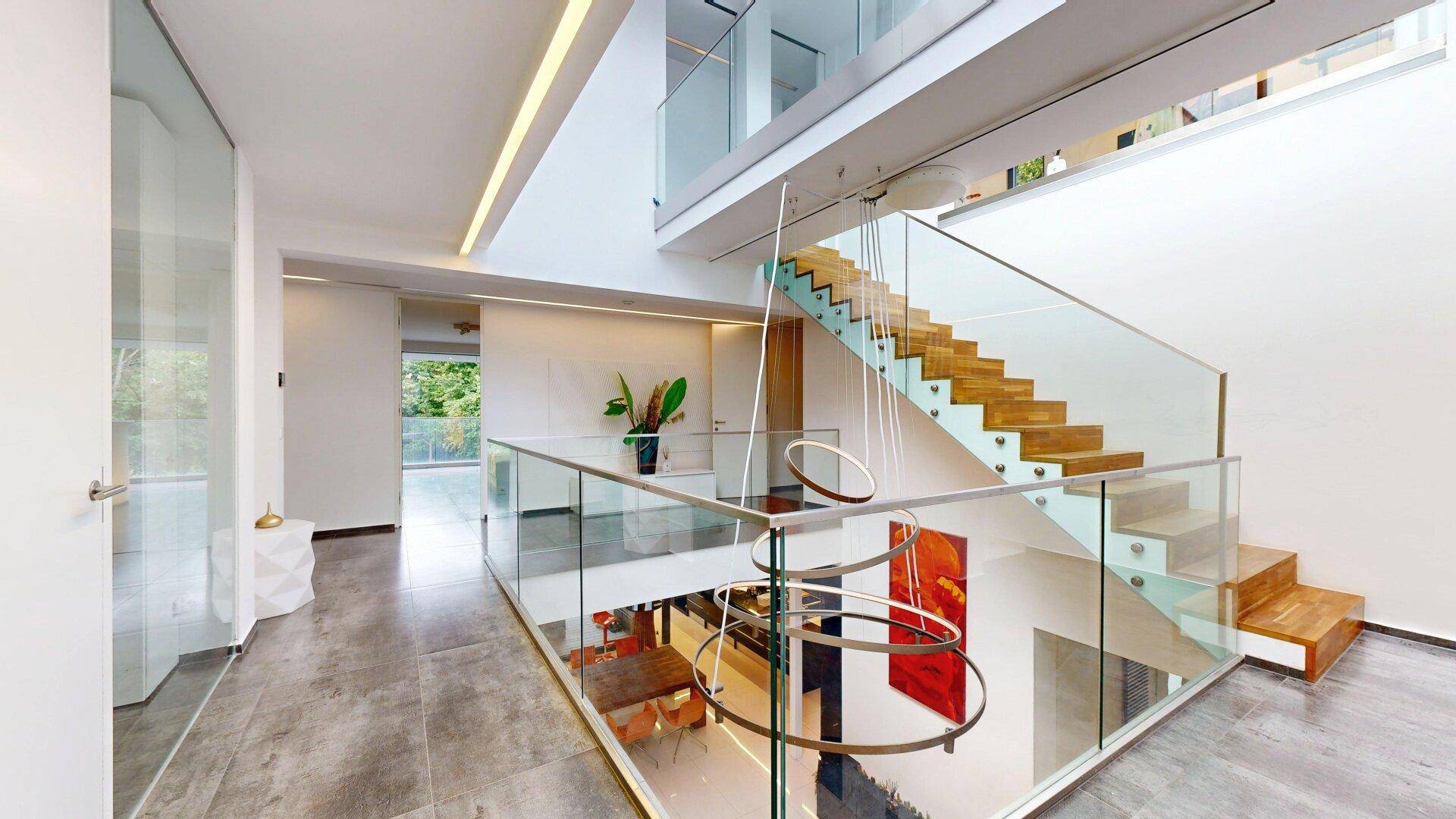 Großzügiger, lichtdurchfluteter Flur mit moderner Treppe, Glasgeländer und Oberlicht.