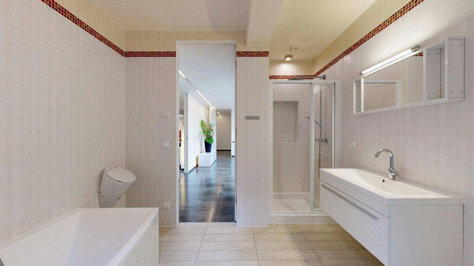 Funktionales Badezimmer mit Dusche, Badewanne und Blick in den hellen Flurbereich.