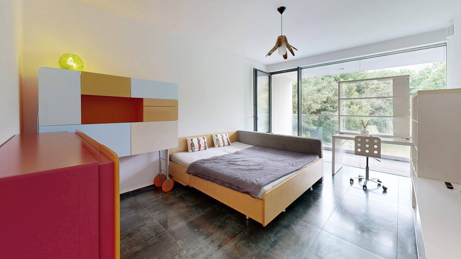 Helles Schlafzimmer mit modernem Bett, Schreibtisch und Zugang zu einem Balkon.