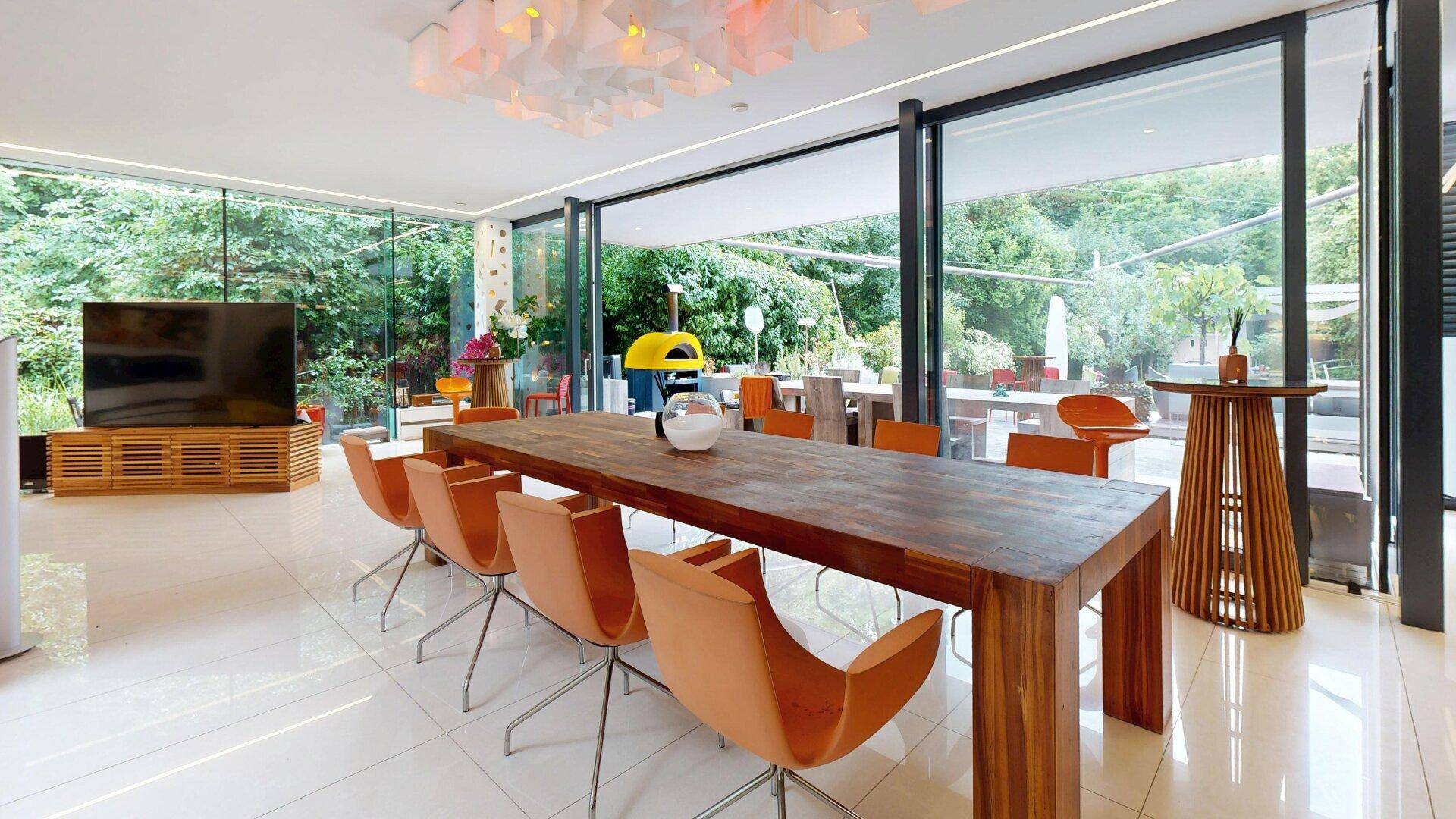 Eleganter Essbereich mit großem Holztisch, orangefarbenen Stühlen und Gartenblick.