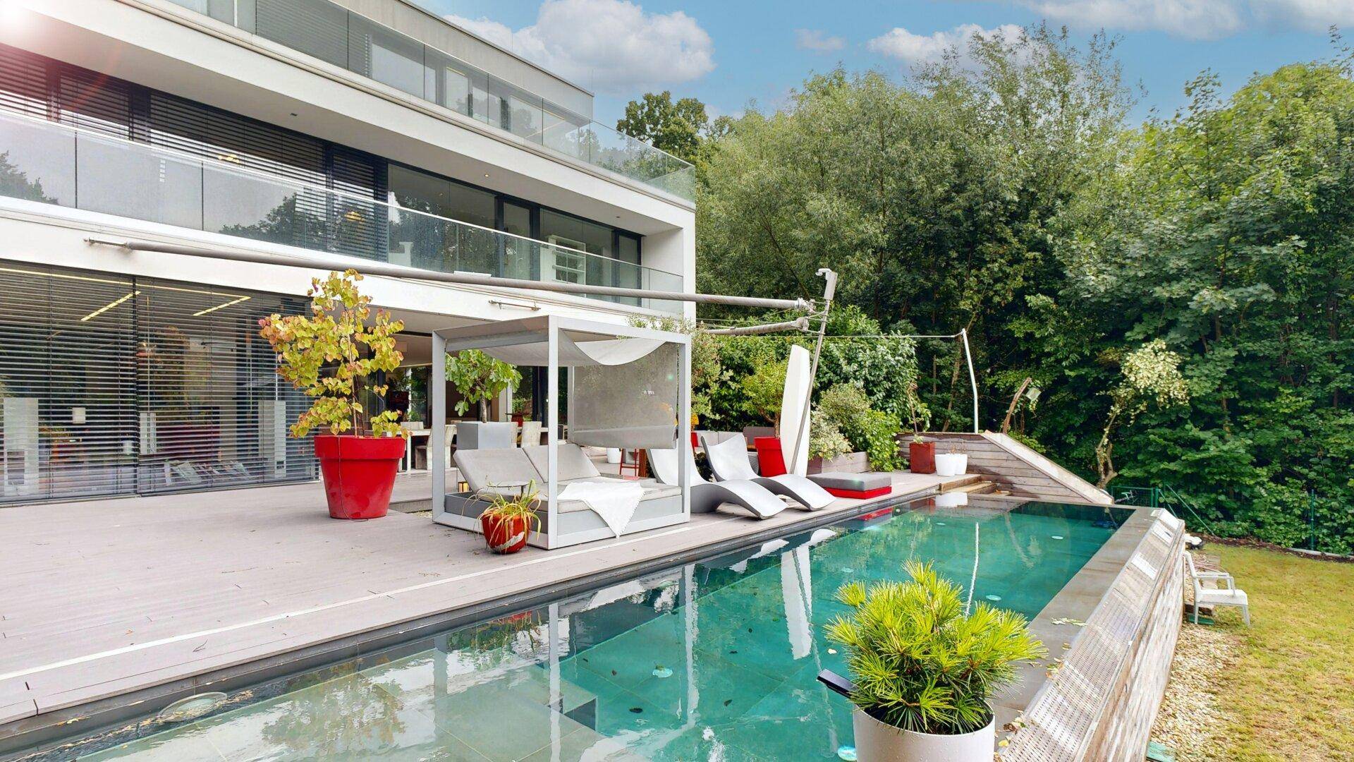 Stilvolle Terrasse mit Pool, Sonnenliegen und moderner Architektur im Hintergrund.