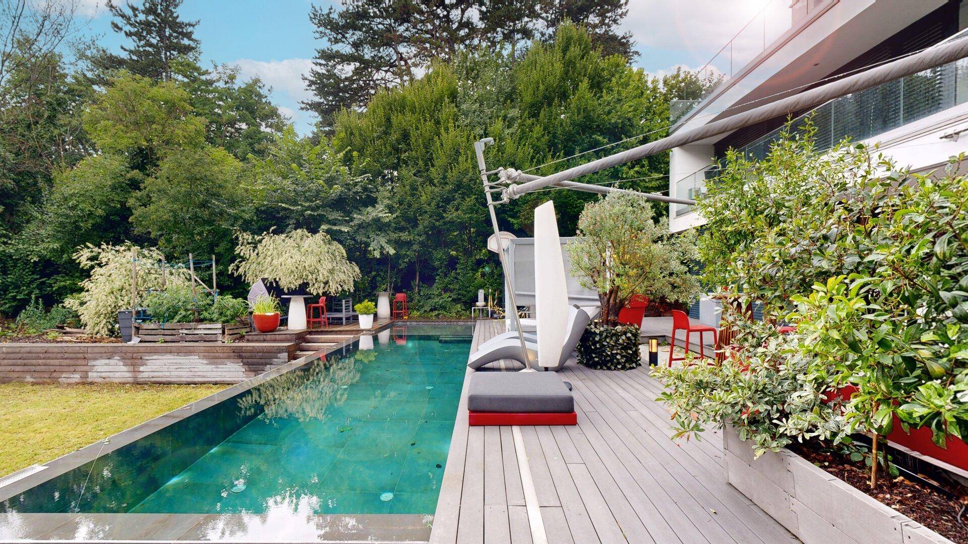 Luxuriöse Terrasse mit Pool, Liegeflächen und üppiger Bepflanzung im Garten.