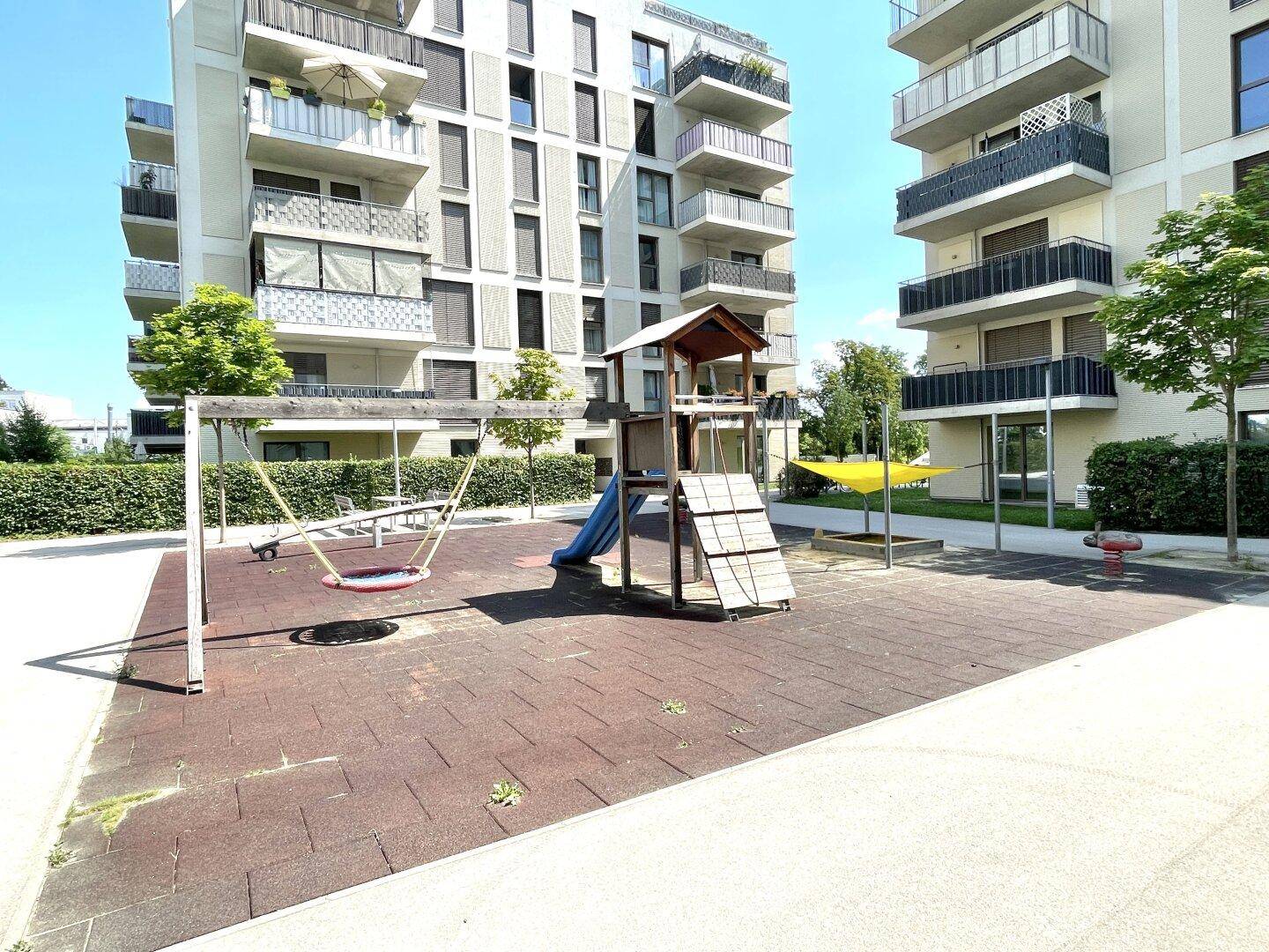 Gemeinschaftlicher Spielplatz mit Rutsche und Schaukeln zwischen modernen Wohngebäuden.
