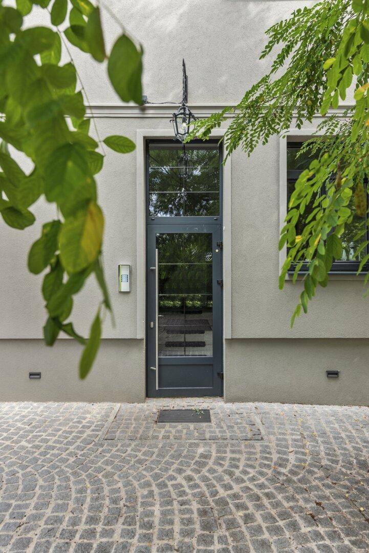 Nahaufnahme der modernen Eingangstür mit Glas und einem historischen Wandleuchter darüber.