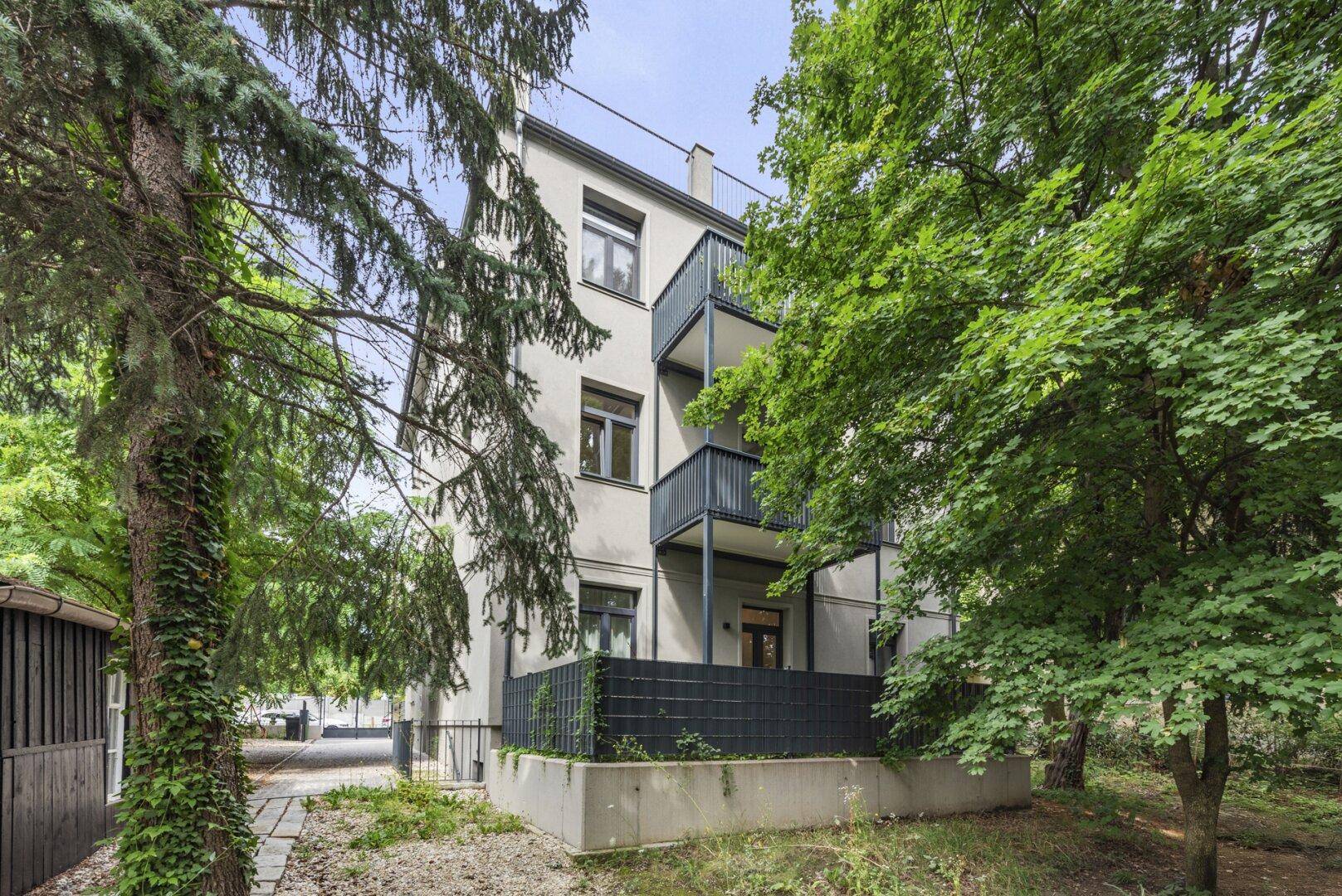 Seitenansicht des Gebäudes mit Balkonen und einem gepflegten Gartenbereich im Vordergrund.