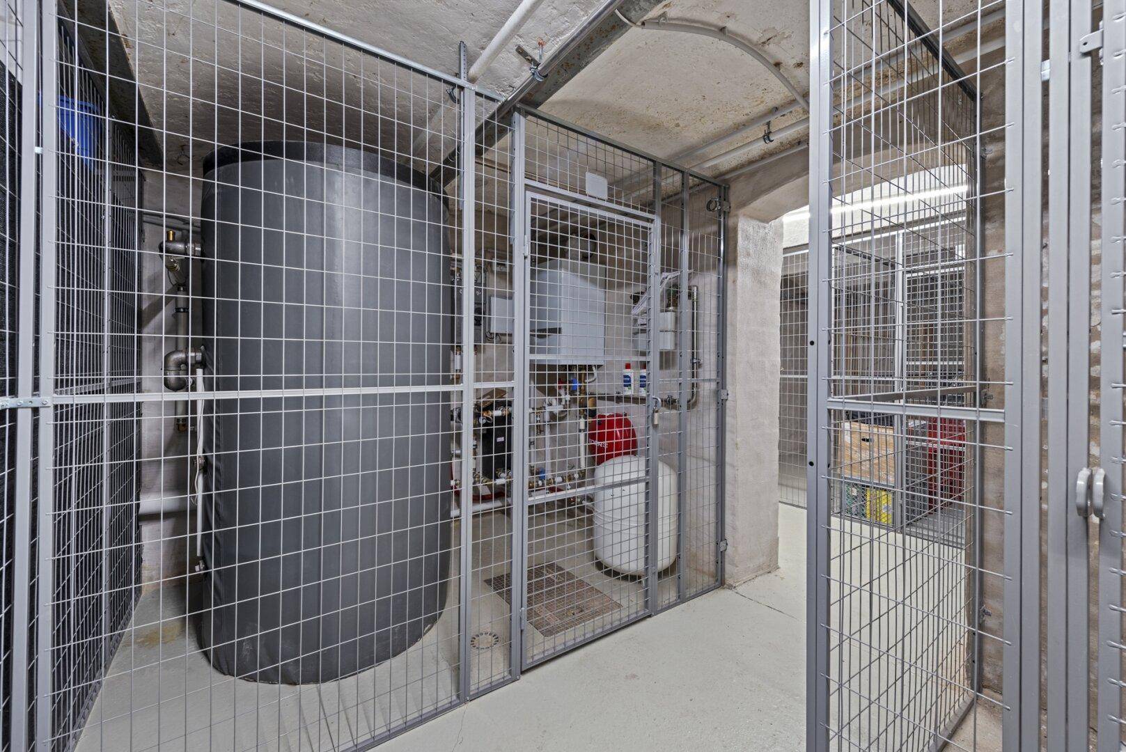 Technikraum im Keller mit Warmwasserspeicher und einzelnen abschließbaren Lagerabteilen.