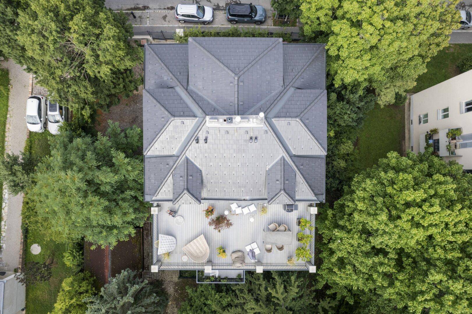 Luftaufnahme eines Gebäudes mit großer Dachterrasse, umgeben von Bäumen und mit Blick auf die Umgebung.