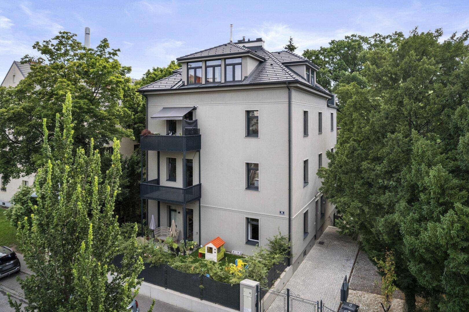 Vorderansicht eines modernen Mehrfamilienhauses mit Balkonen und einem kleinen Spielbereich im Vorgarten.