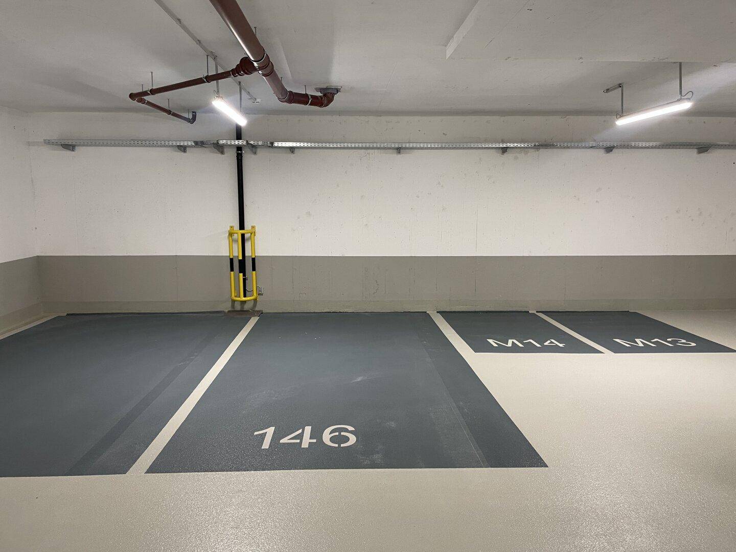Tiefgarage mit markierten Parkplätzen und sichtbaren Versorgungsleitungen an der Decke.
