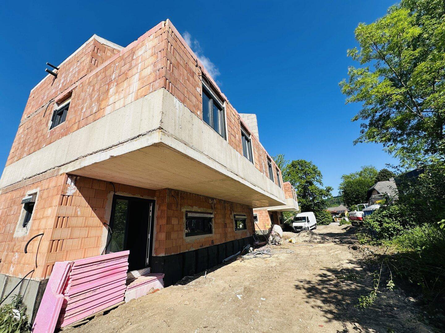 Rohbau eines modernen Wohnhauses mit Ziegelmauerwerk und großen Fensteröffnungen in sonniger Umgebung.