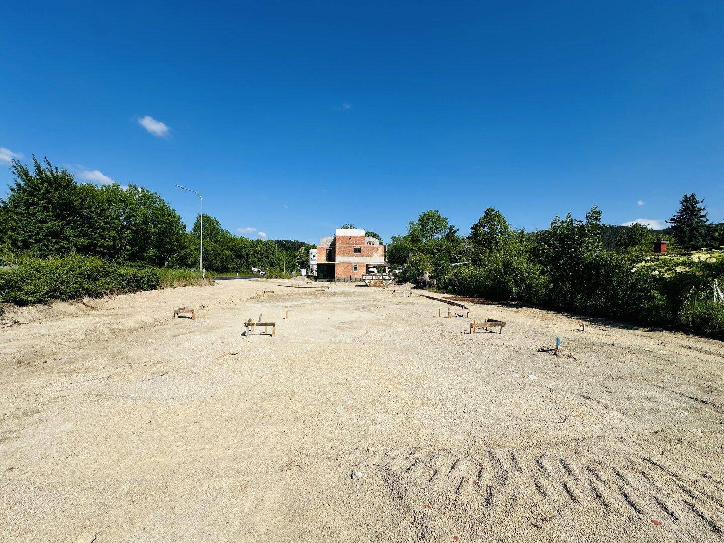 Großes Baugrundstück mit dem Rohbau-Gebäude im Hintergrund und viel Freifläche.