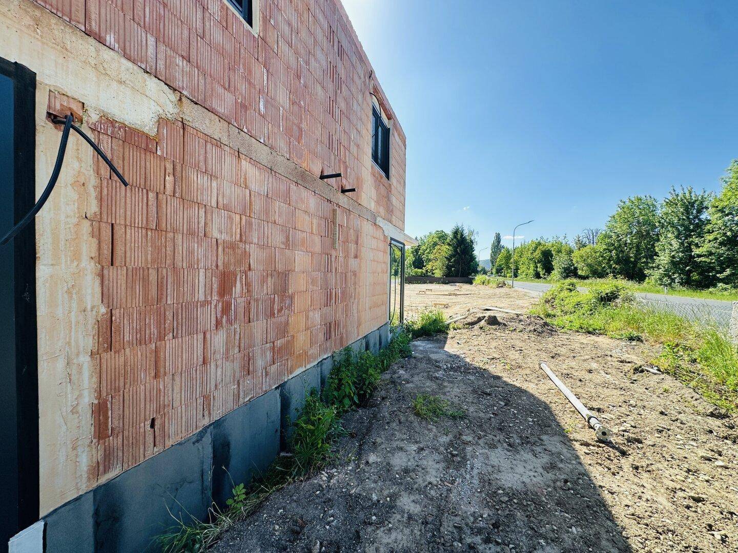 Blick entlang der Hauswand im Rohbauzustand mit sichtbarem Fundament und Erdboden.
