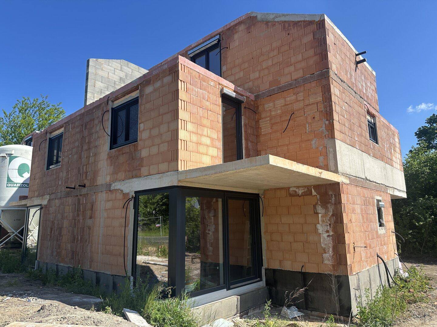 Detailansicht des Neubaus mit Ziegelwänden, großen Fenstern und Betonstrukturen.