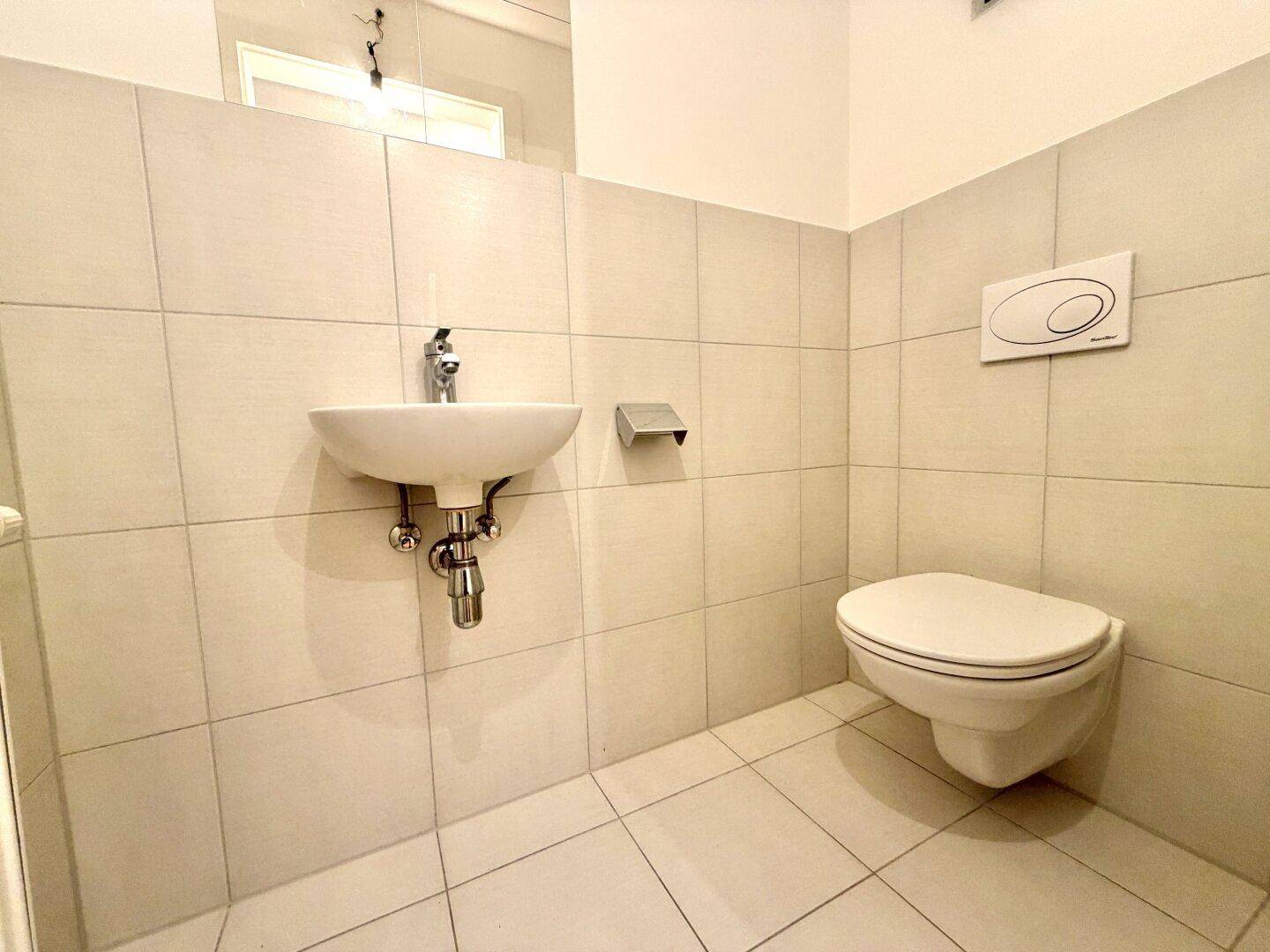 Kleines Gäste-WC mit Waschbecken und wandhängender Toilette, hell gefliest.