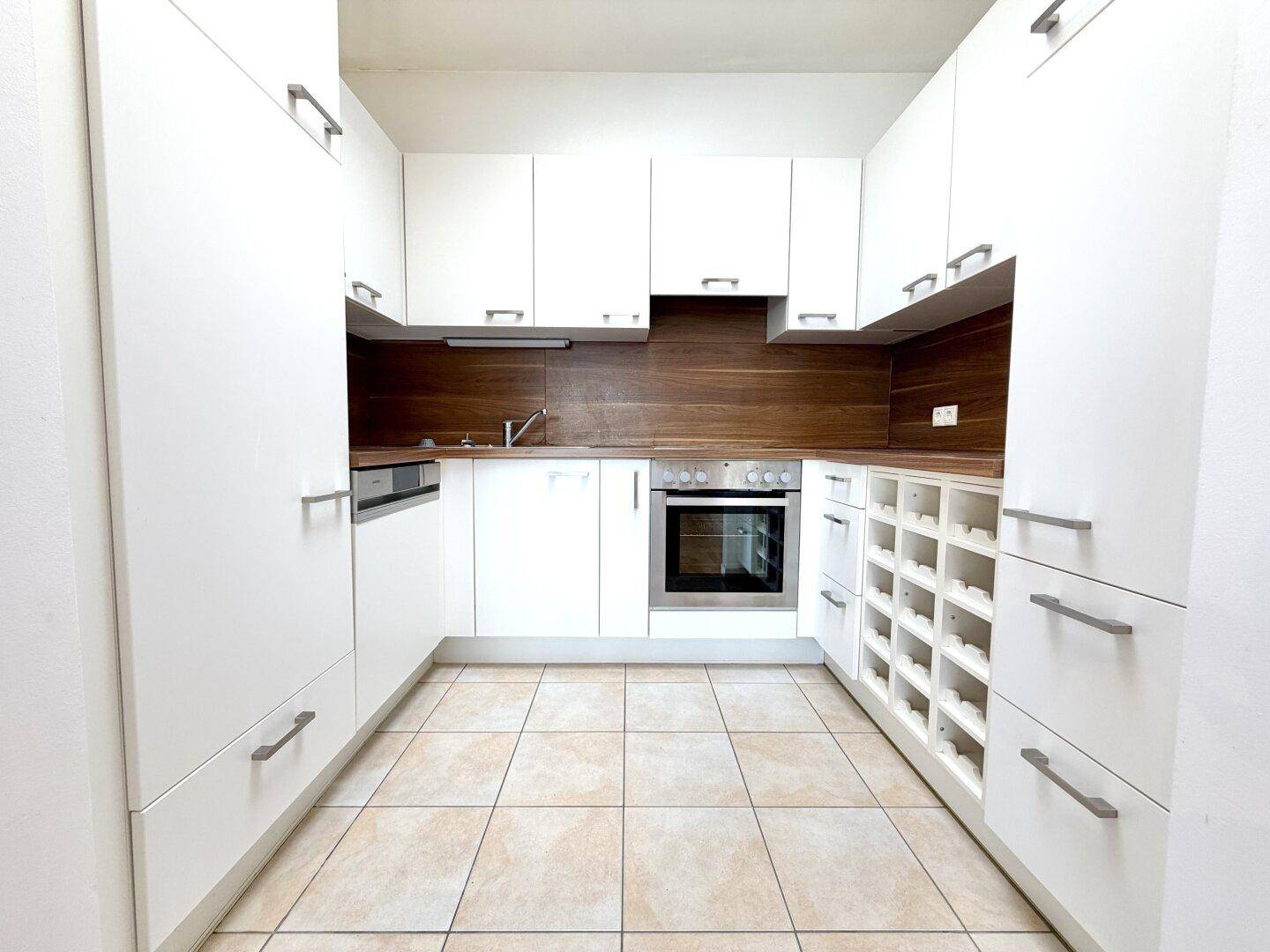 Funktionale Einbauküche mit weißen Schränken, Holzdetails und Fliesenboden.
