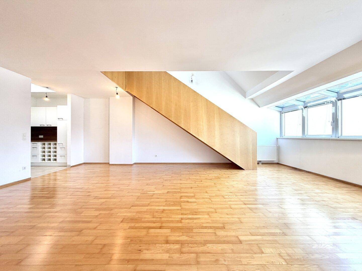 Offener Wohnbereich mit Holzparkett, moderner Holztreppe und viel Tageslicht.