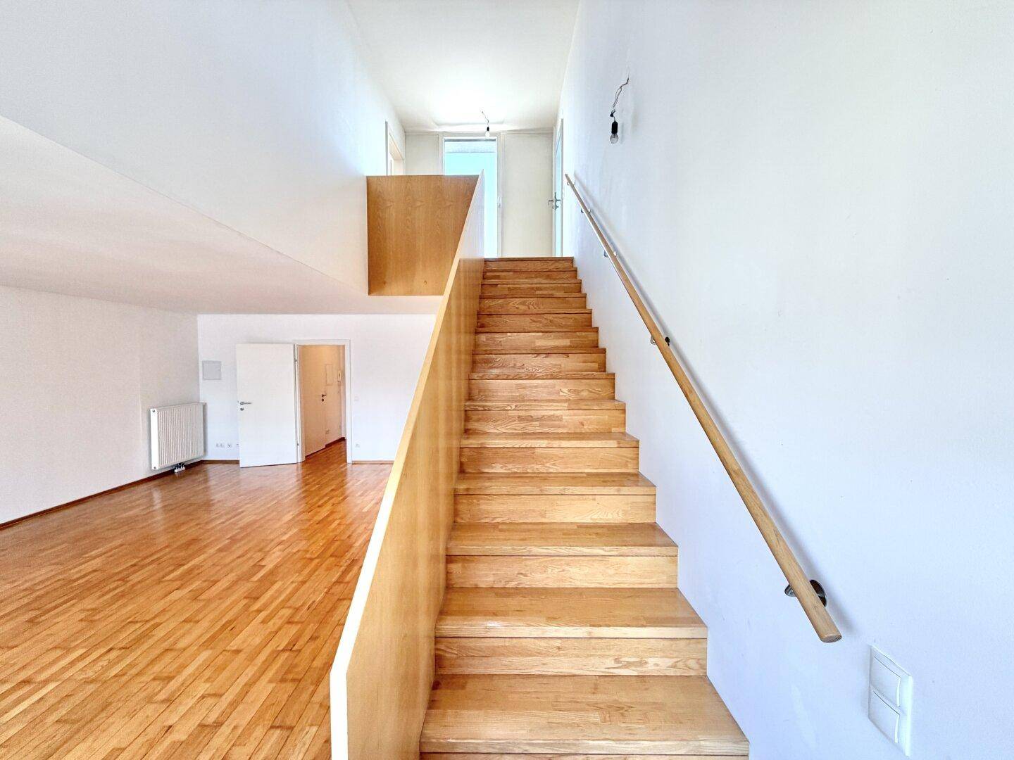 Moderne Holztreppe mit Handlauf in einem hellen Flurbereich mit Parkettboden.
