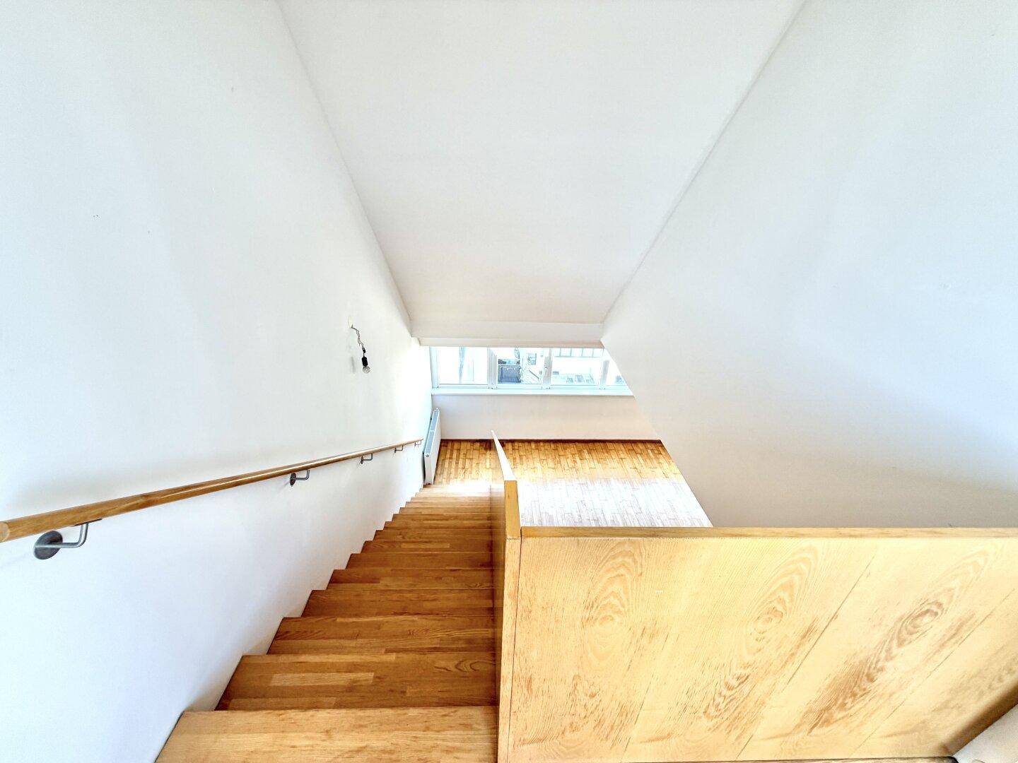 Blick von oben auf die helle Holztreppe, die in den unteren Wohnbereich führt.