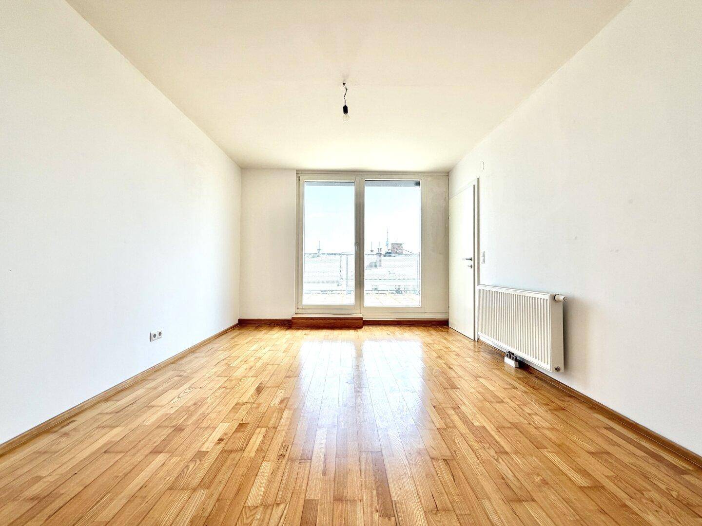Helles Zimmer mit Holzparkettboden und Zugang zu einem französischen Balkon.