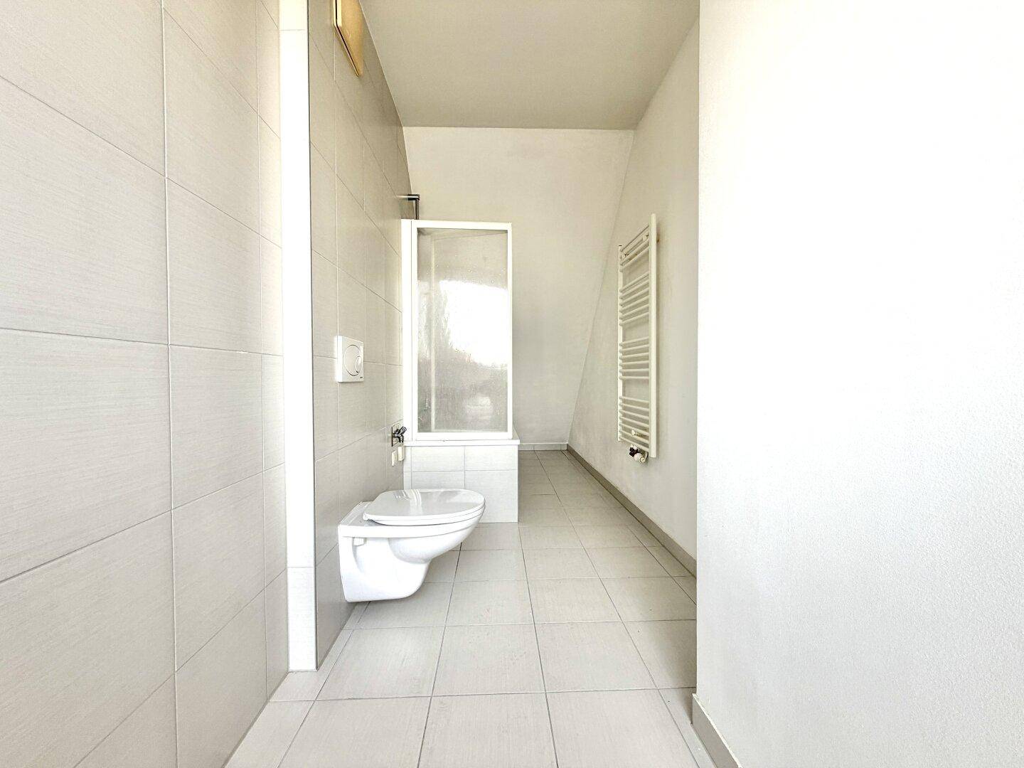 Helles Badezimmer mit Dusche, wandhängendem WC und beheiztem Handtuchhalter.