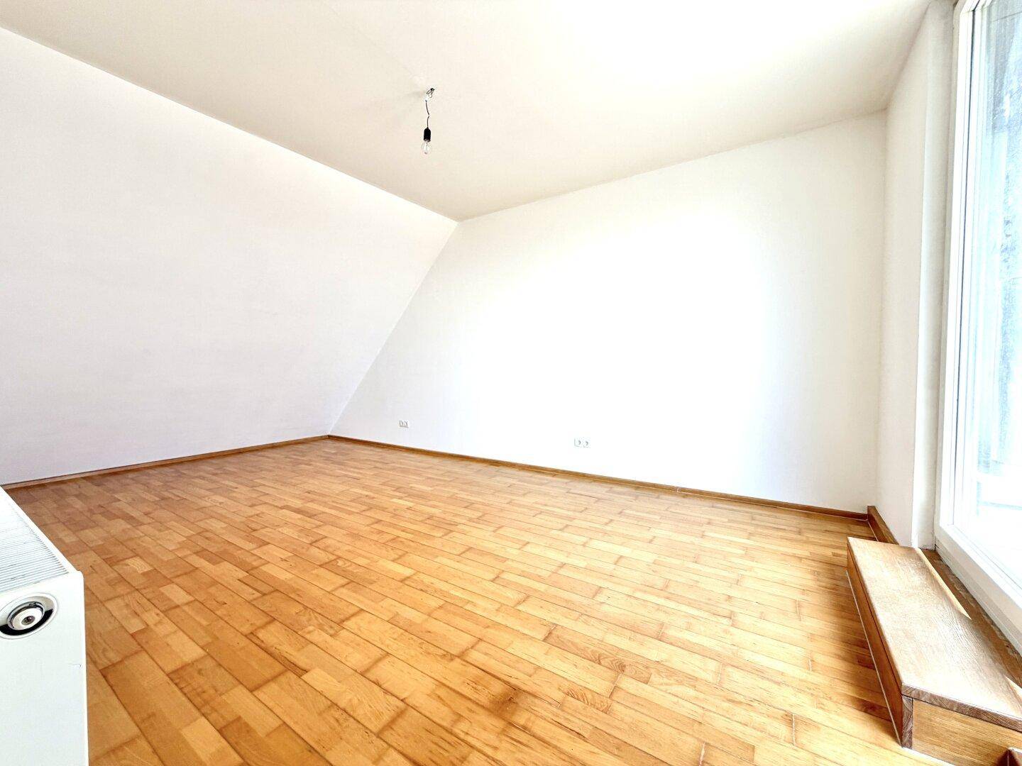 Geräumiges Zimmer mit Holzparkett, Dachschräge und viel natürlichem Licht.