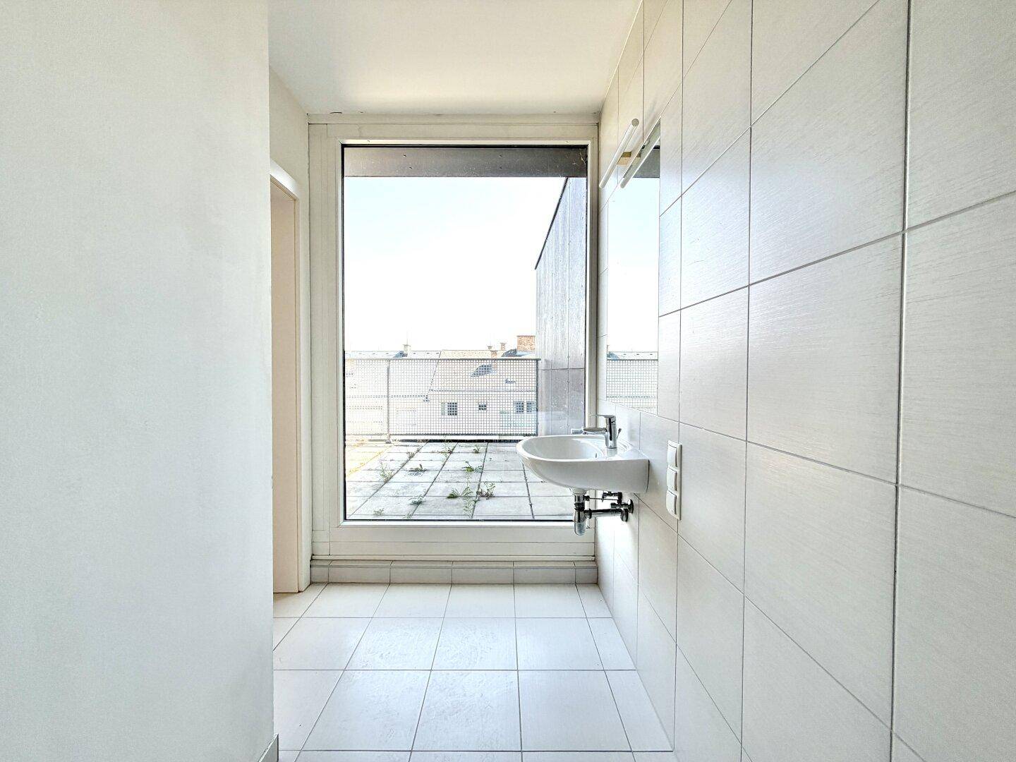 Modernes Badezimmer mit großem Fenster, Waschbecken und hellen Fliesen.