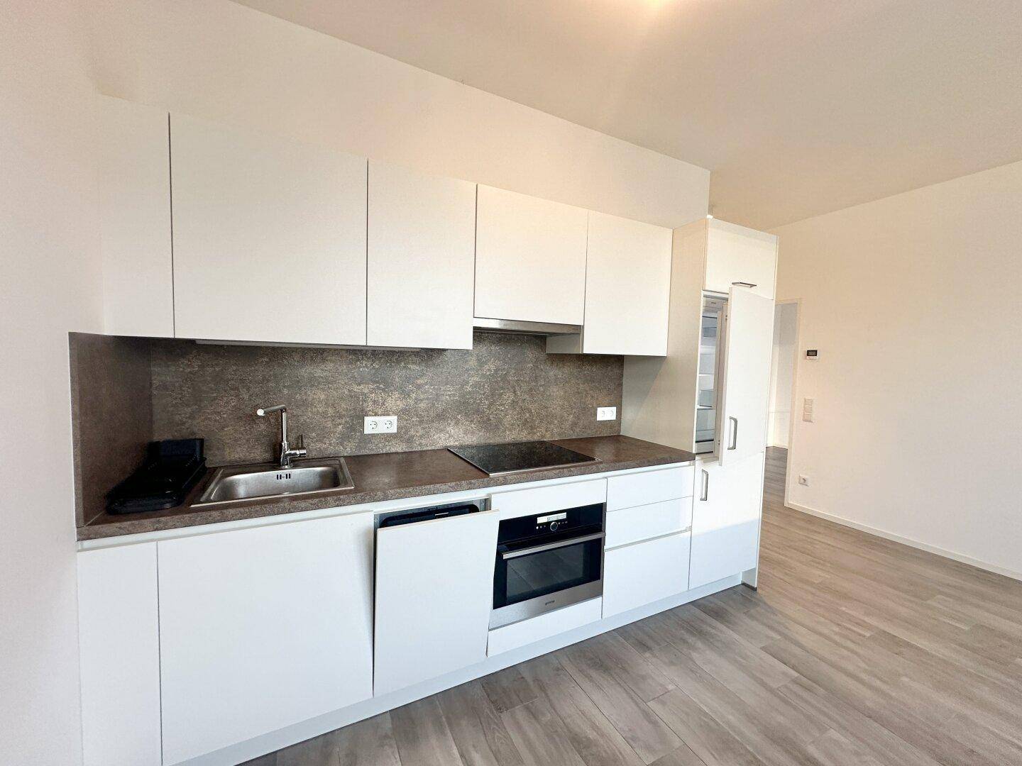 Moderne Küchenzeile mit weißen Schränken, Induktionskochfeld und integriertem Backofen.