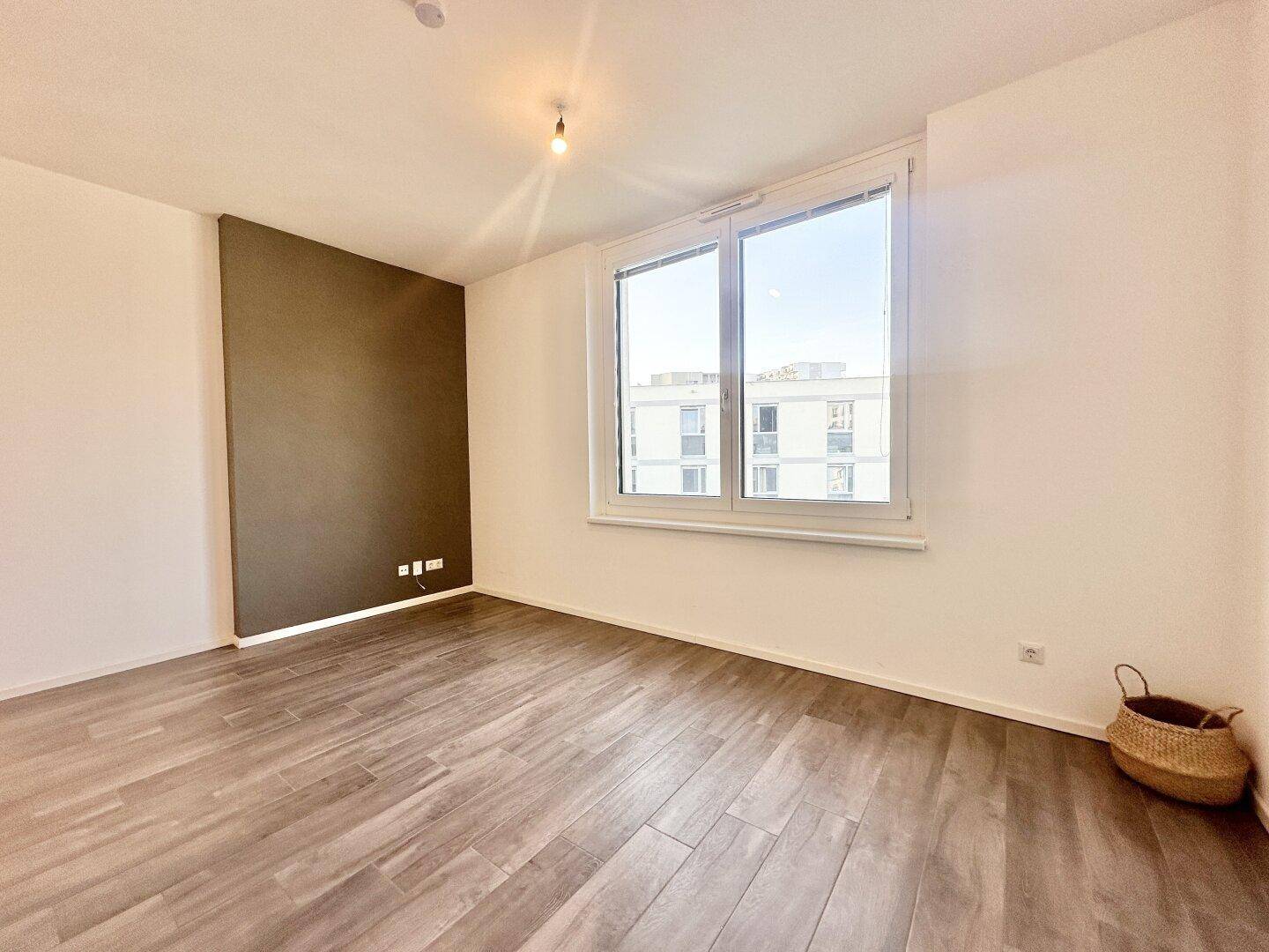 Helles Schlafzimmer mit großem Fenster, modernem Boden und einer Akzentwand in Erdtönen.