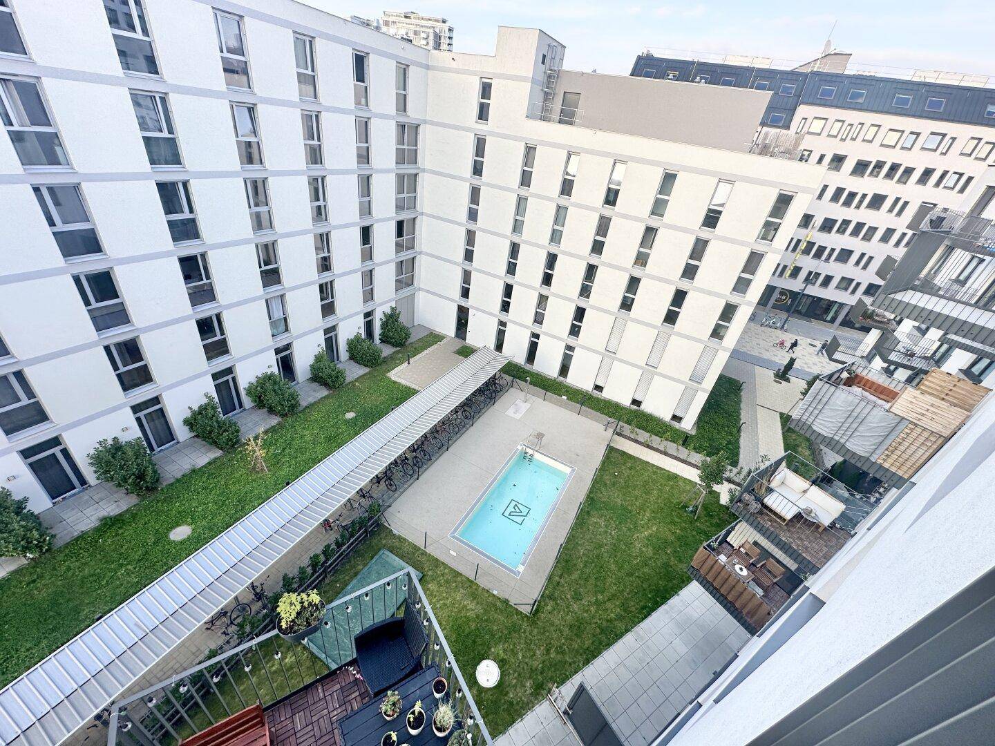 Luftaufnahme eines modernen Wohnkomplexes mit Innenhof, Rasenflächen und einem kleinen Pool.