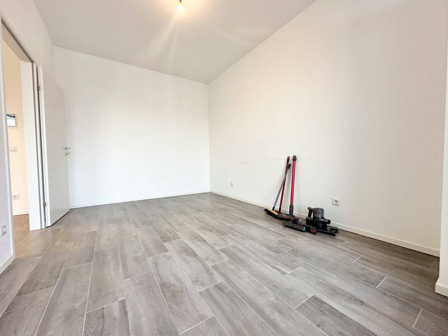 Heller, leerer Raum mit modernen grauen Fliesen in Holzoptik und hohen Decken.