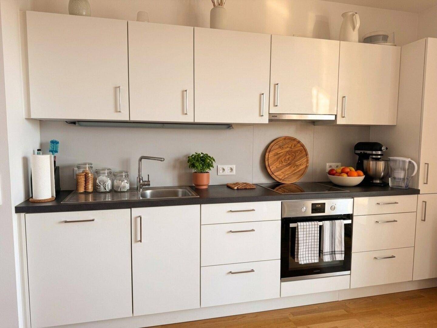 Moderne Einbauküche mit weißen Schränken, dunkler Arbeitsplatte und integrierten Geräten.