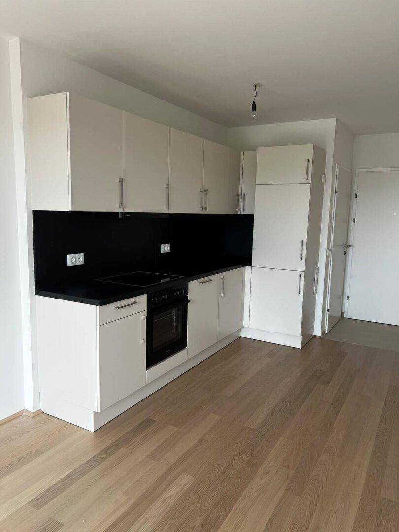 Moderne Einbauküche mit weißen Schränken, schwarzer Arbeitsplatte und hellem Holzfußboden in einem leeren Raum.